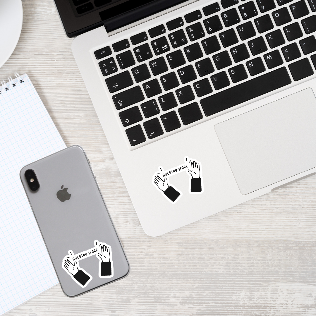 Matte vinyl sticker featuring two hands holding a banner that reads ‘HOLDING SPACE’ displayed on a laptop, showcasing its meaningful design